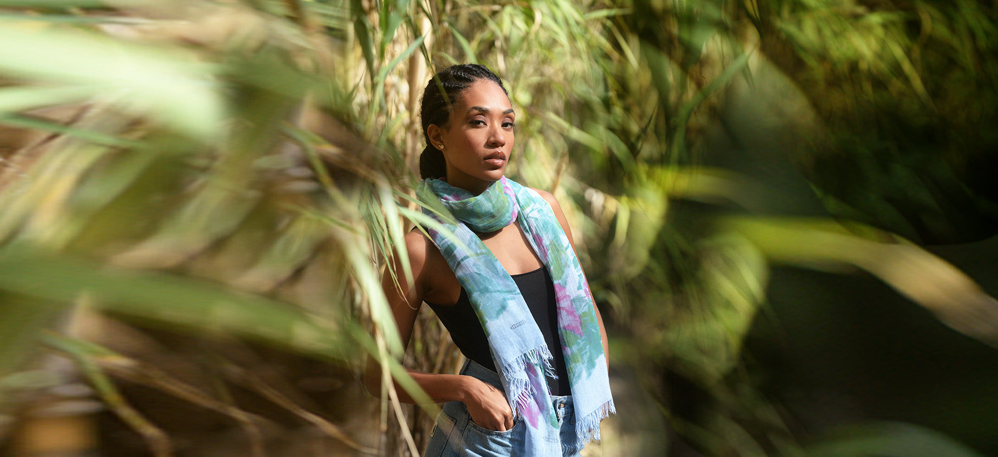 Ragazza che indossa Foulard Bamboo Boldini con delle piante di bambù intorno sfocate e che lasciano intravedere la ragazza al centro. 